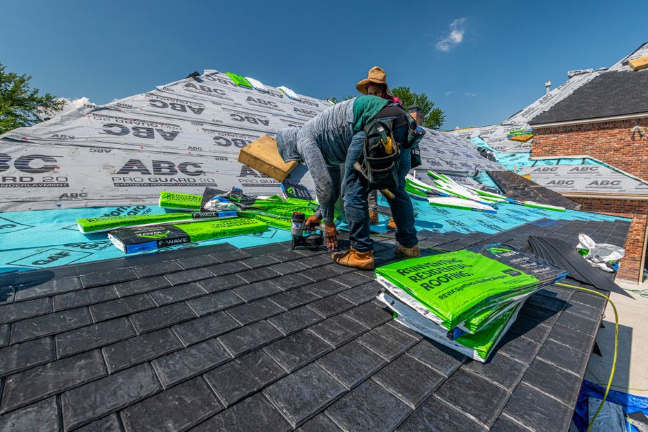 Roofers installing a new slate roof on a brick house