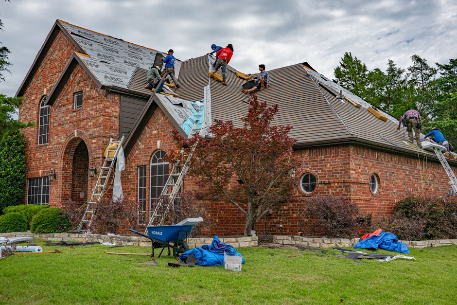 Roofers working together on the roof of a brick home