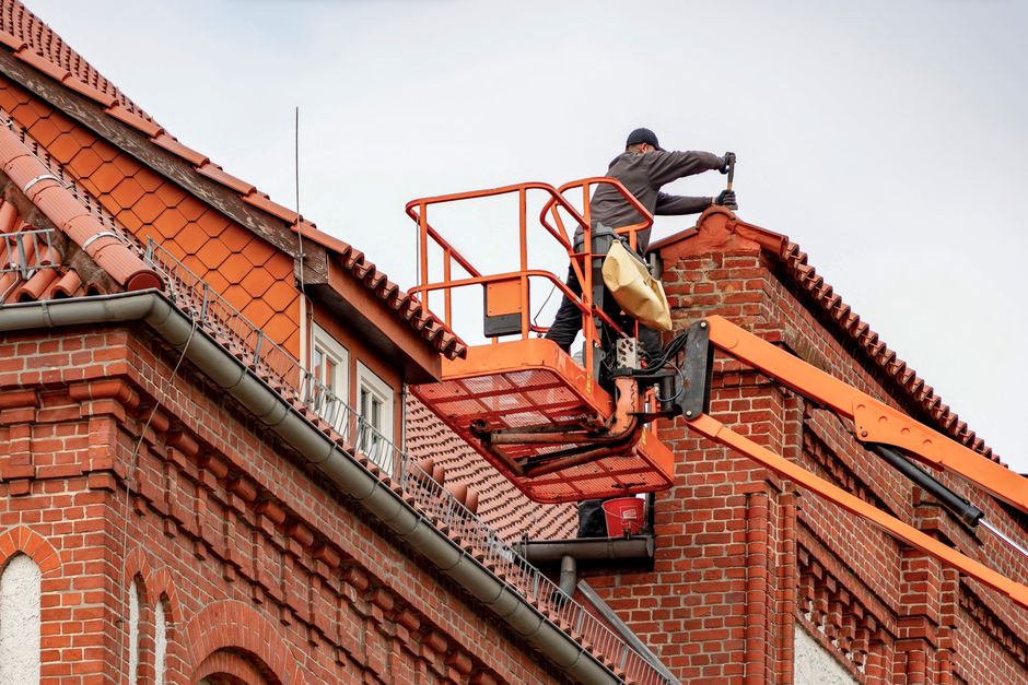 A roofer working from a cherry picker at a brick building